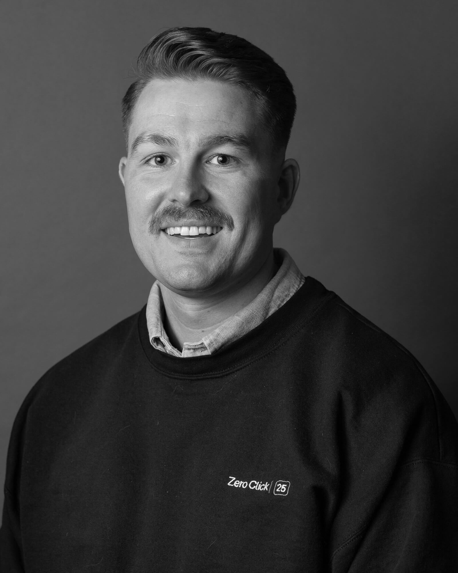 Black and white portrait of a smiling man with a mustache, wearing a "Zero Click" sweatshirt.