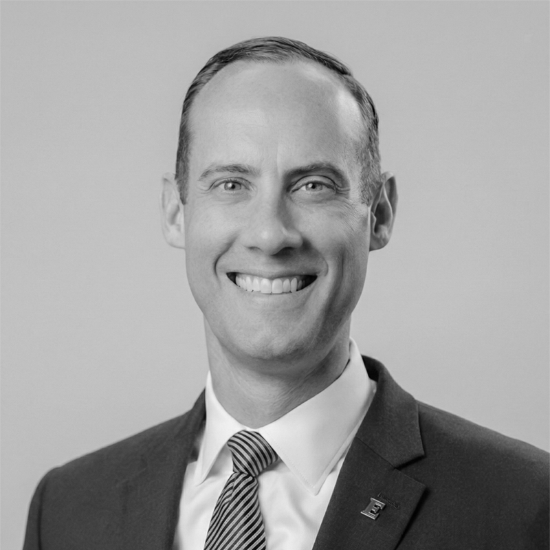 Smiling man in a suit and tie posing for a professional headshot against a plain background.