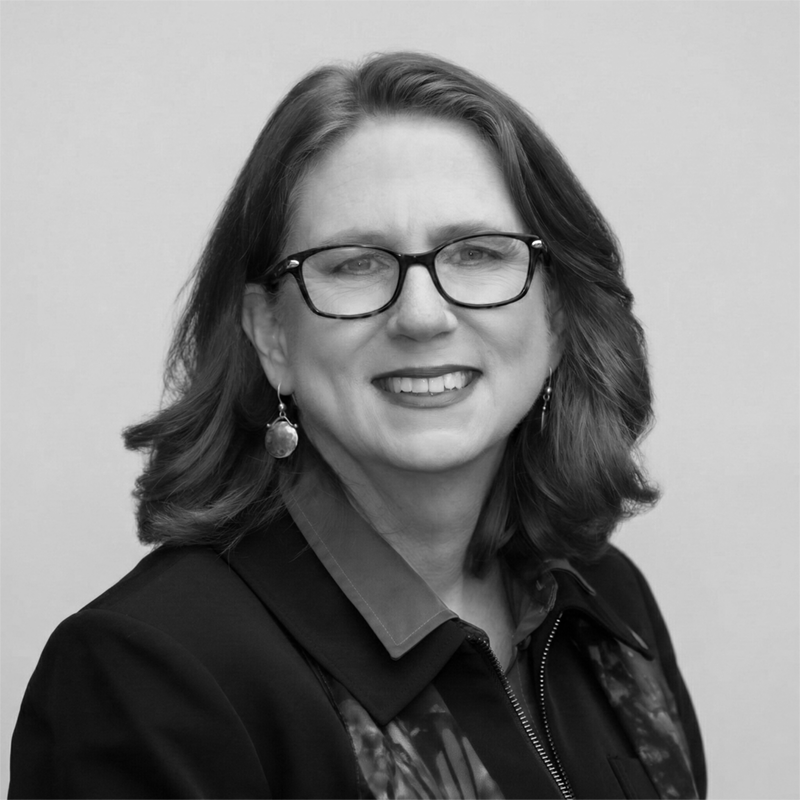 Woman with shoulder-length hair and glasses, wearing earrings and a jacket, smiling at the camera.