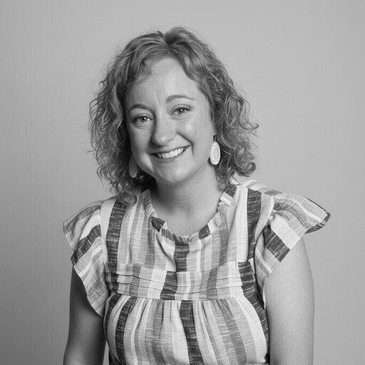 Smiling woman with curly hair in a striped shirt posing against a plain background, in black and white.