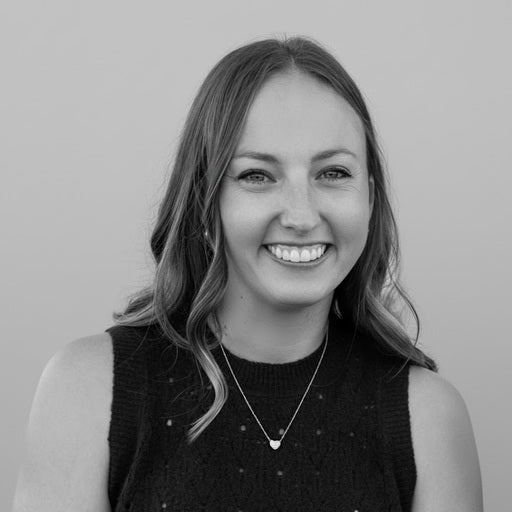 Smiling woman with long hair, wearing a sleeveless top and necklace, in front of a plain background.