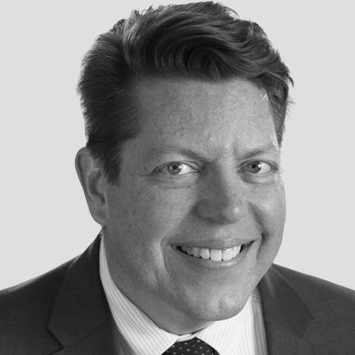 Smiling man in a suit and tie, shown from the shoulders up, with a neutral background.