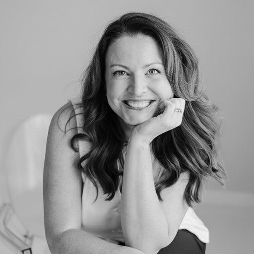Smiling woman with long hair rests her chin on her hand, sitting in a bright room. Black and white photo.