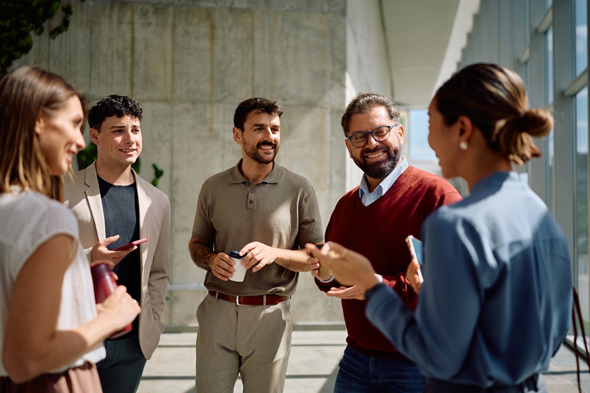 Five people in business attire smiling and talking together in a bright, modern office space.