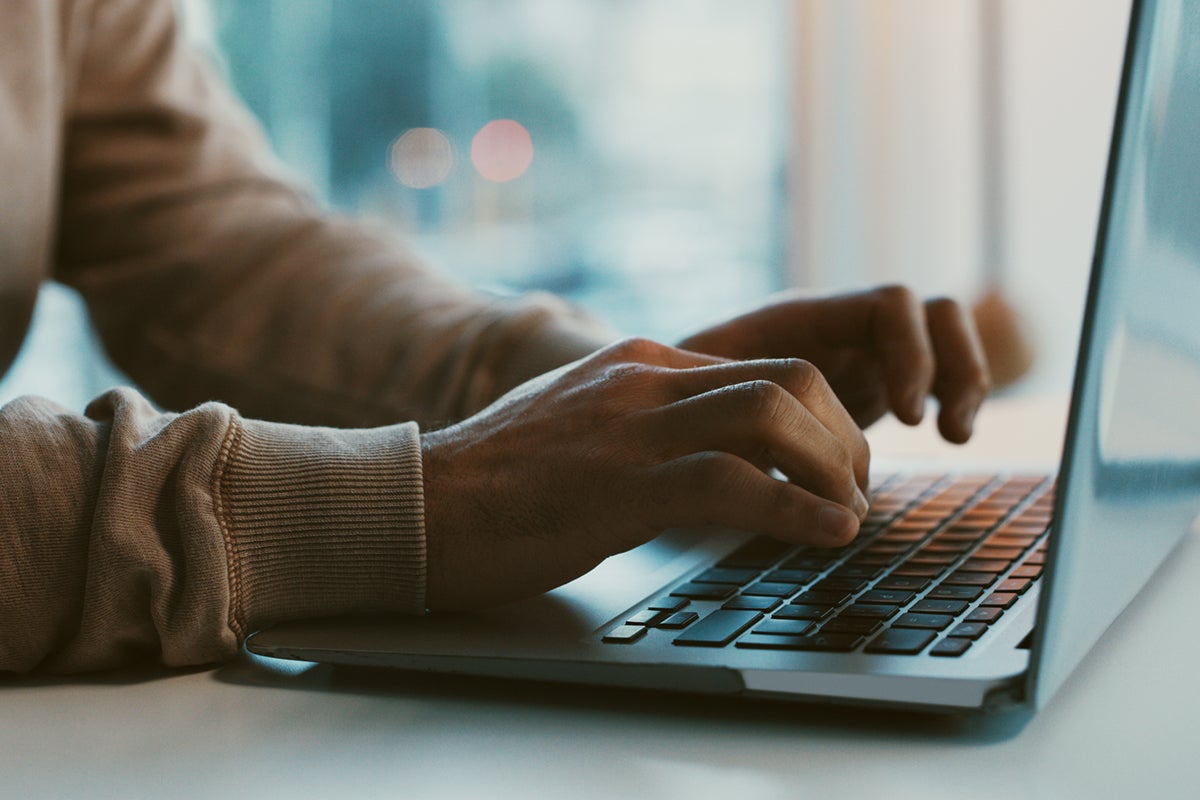 Close-up of a person typing on a laptop keyboard at a desk with soft natural light.
