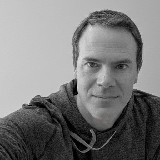 Man in a hoodie looking at the camera and smiling slightly, black and white portrait.