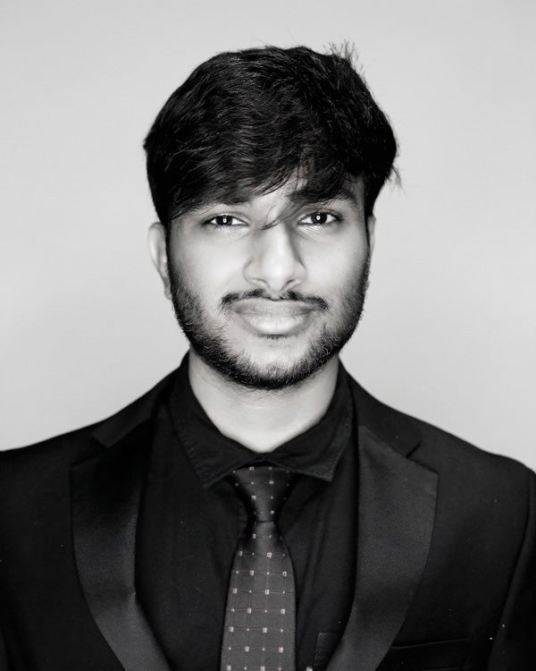 A man in a suit and tie smiles slightly while facing the camera against a plain background.