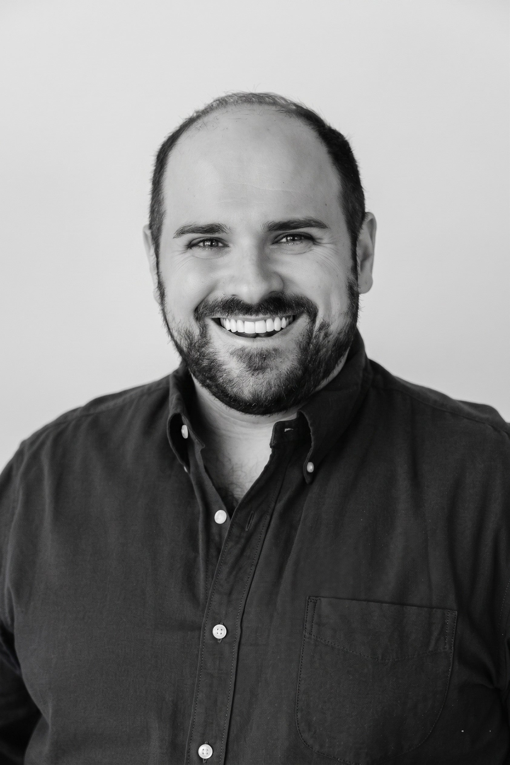 Smiling man with a beard and dark shirt, facing forward with a neutral background.