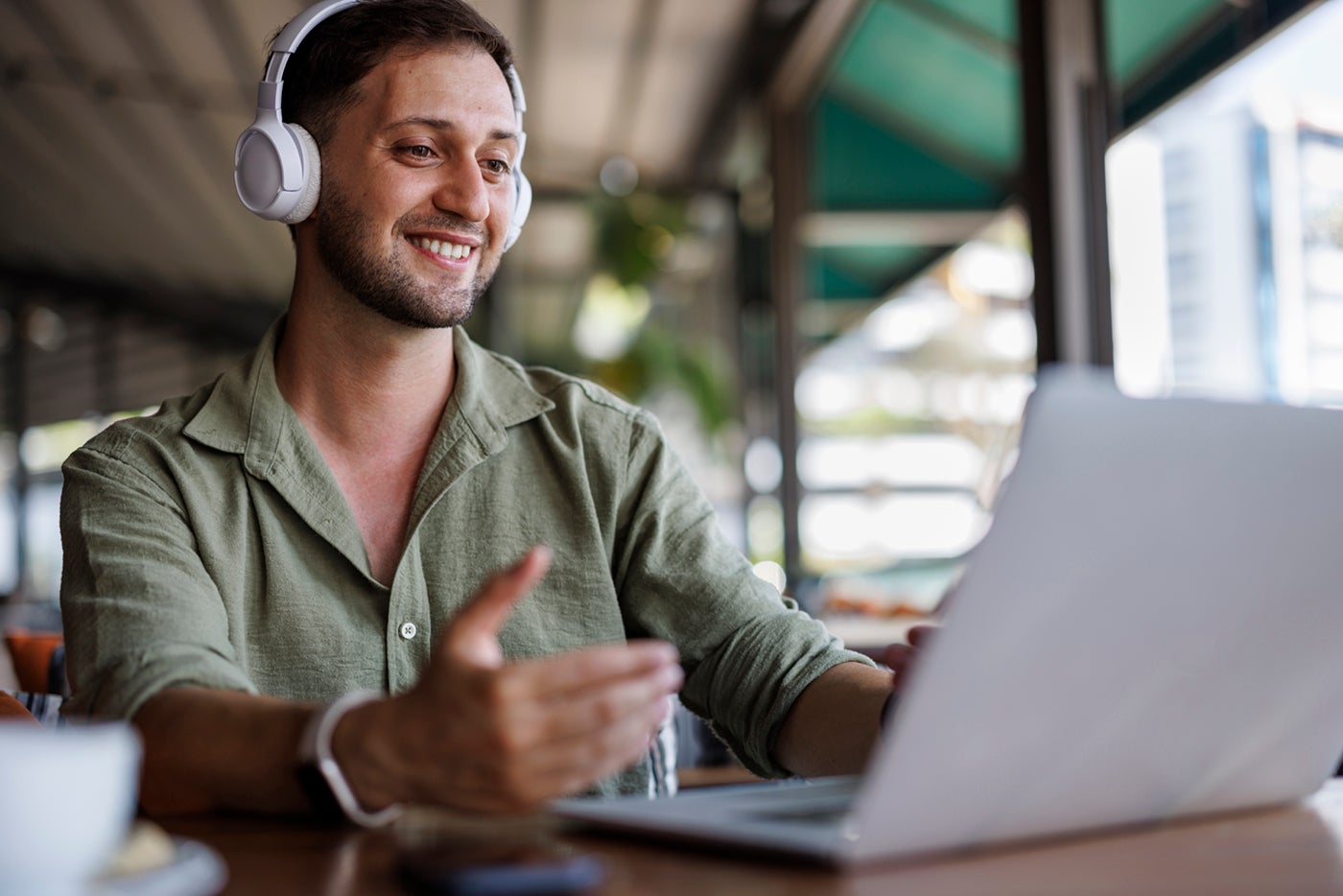 A smiling man wearing headphones gestures while video chatting on a laptop.